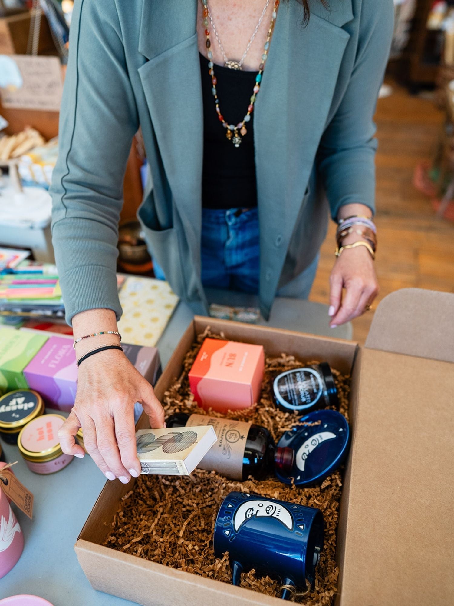 Bella Vita team member in teal blazer curating a personalized gift box with handpicked wellness products and handcrafted items