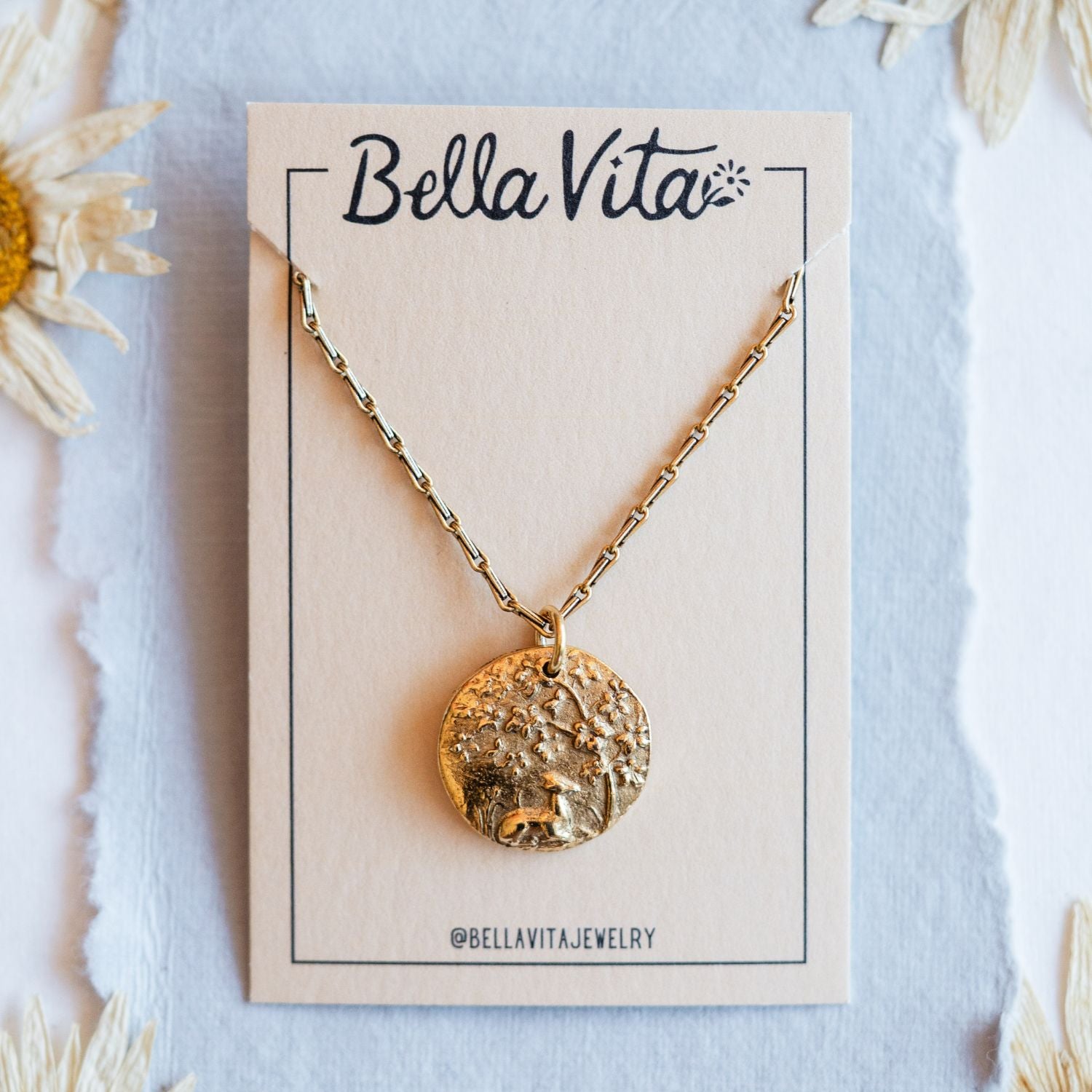 Gold cast fawn heirloom pendant displayed on Bella Vita branded card with daisy flowers