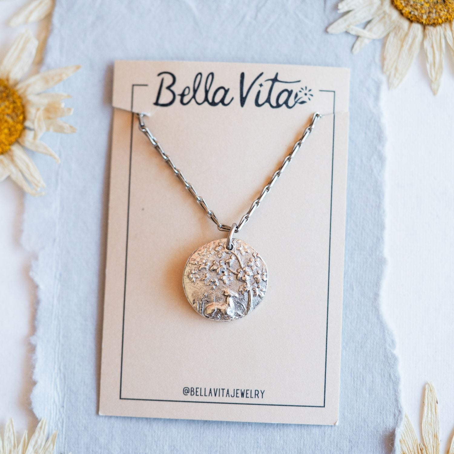Silver cast fawn heirloom pendant shown with Bella Vita artisan jewelry packaging and daisies
