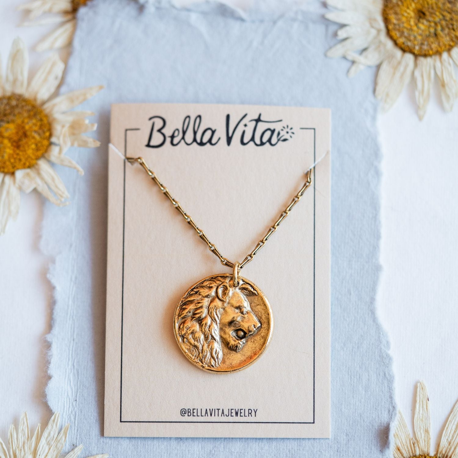 Gold cast lion heirloom pendant displayed on Bella Vita branded card with daisy flowers