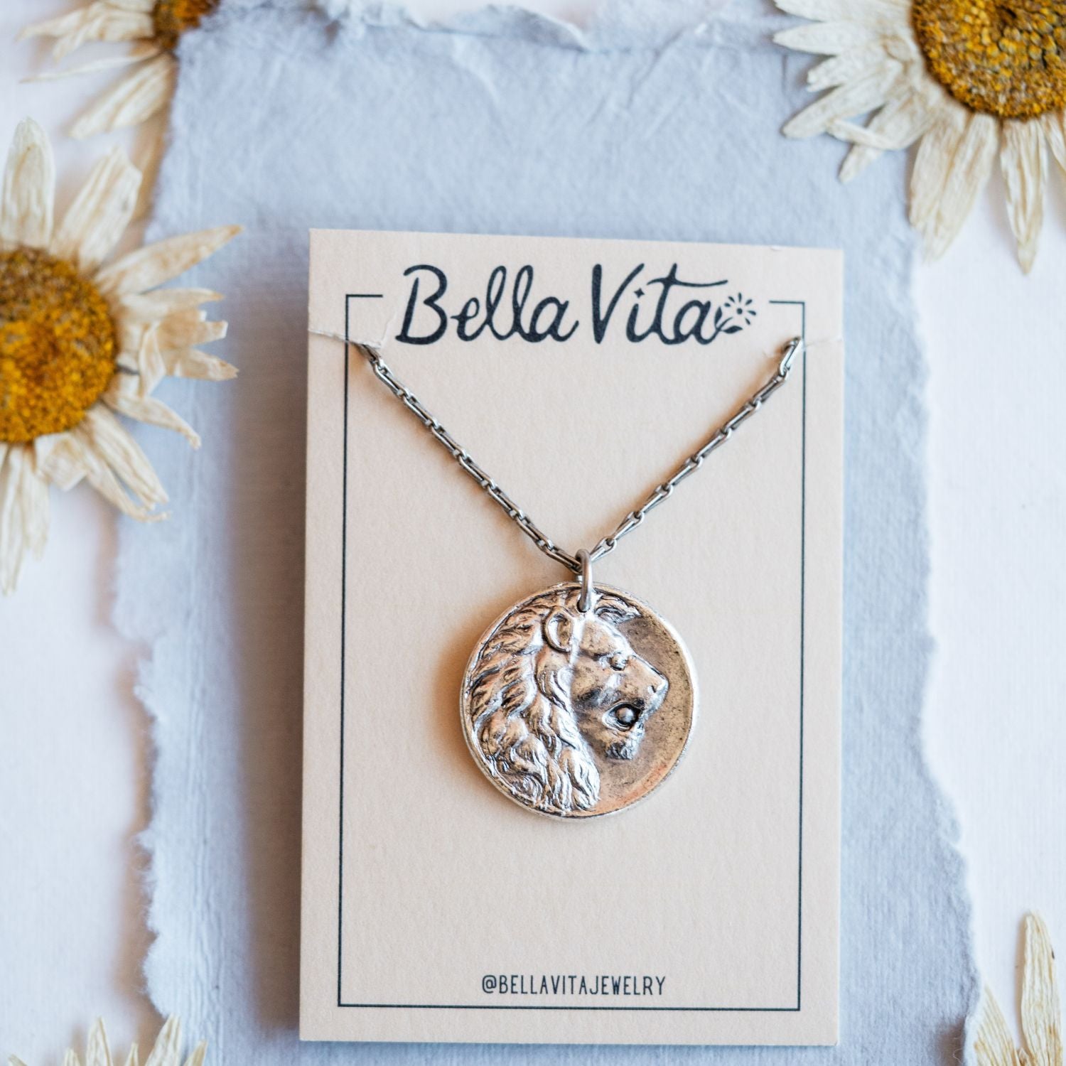 Silver cast lion heirloom pendant shown with Bella Vita artisan jewelry packaging and daisies
