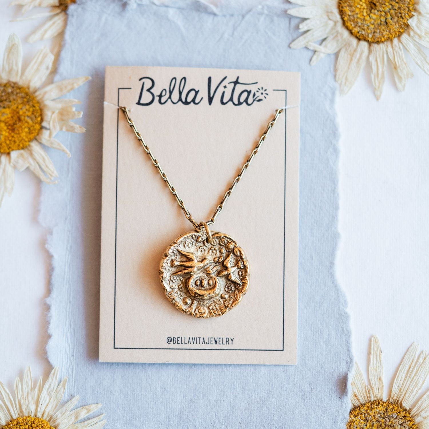 Gold cast mama bird heirloom pendant displayed on Bella Vita branded card with daisy flowers