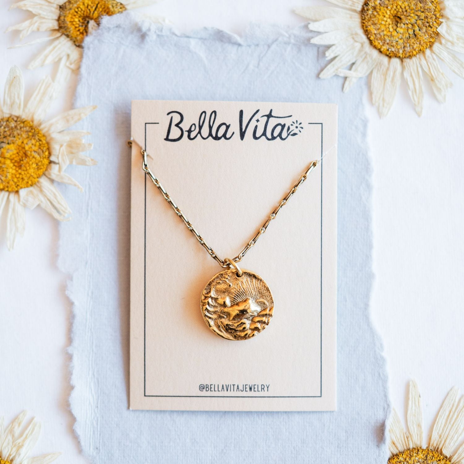 Gold cast mountain sunset heirloom pendant on Bella Vita branded card with daisy flowers