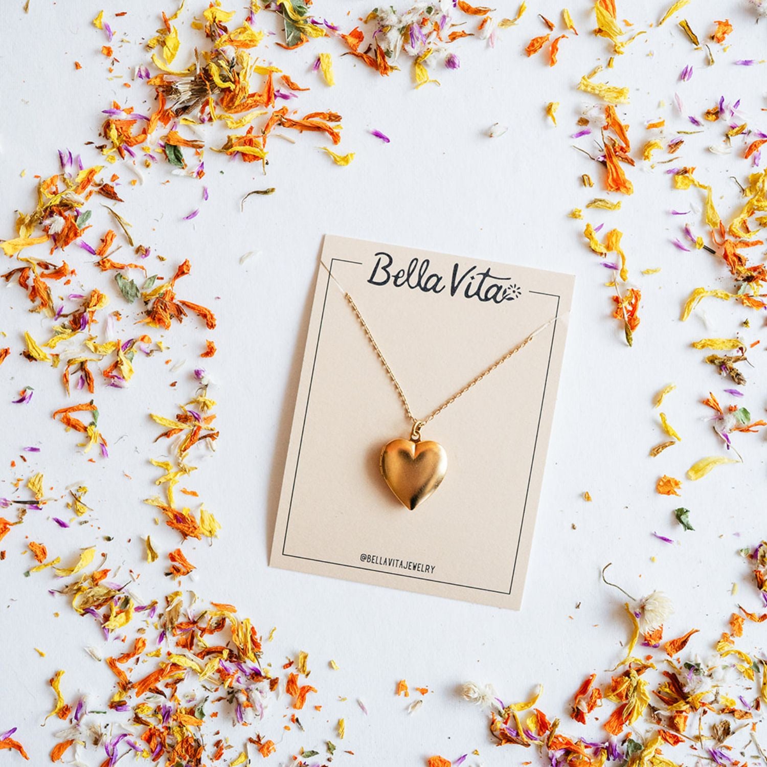 Bella Vita's gold heart pendant necklace handcrafted in our Little Rock studio, displayed on a branded card encircled by colorful dried flower petals, creating a meaningful keepsake.