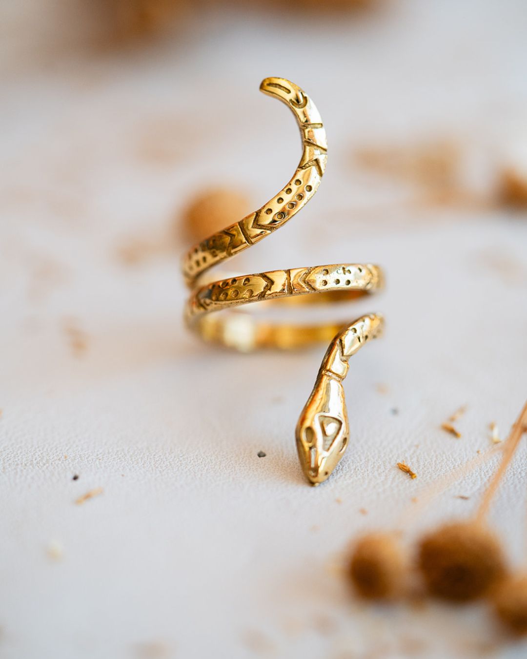 Patterned brass serpent ring on white surface showing detailed snake coil design