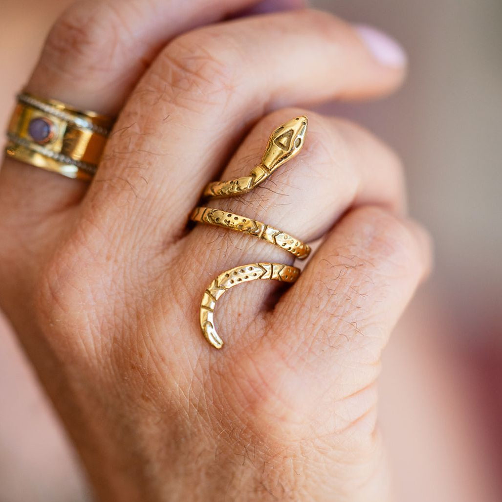 Hand wearing adjustable patterned brass serpent ring with mixed metal jewelry