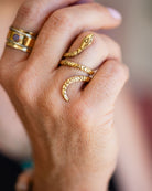 Hand wearing adjustable patterned brass serpent ring with mixed metal jewelry