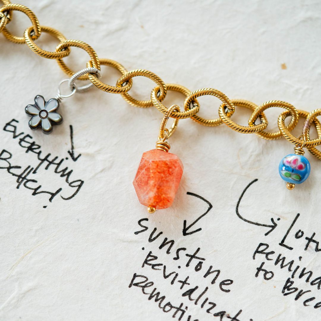 Custom charm bracelet design process showing gold chain with handwritten notes and gemstone charm placement