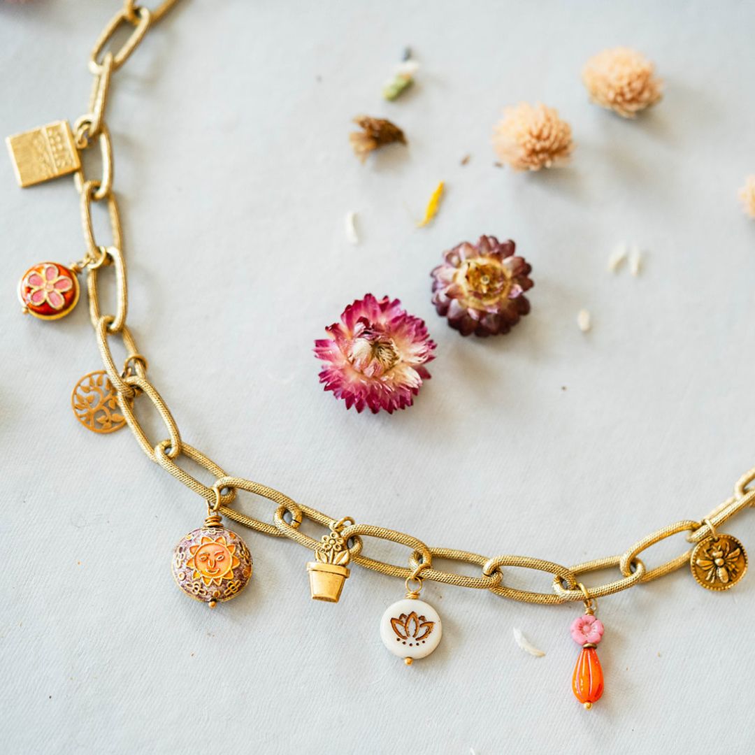 Close-up of gold charm necklace featuring detailed sun charm, lotus flower, and garden-themed enamel charms with dried flower styling