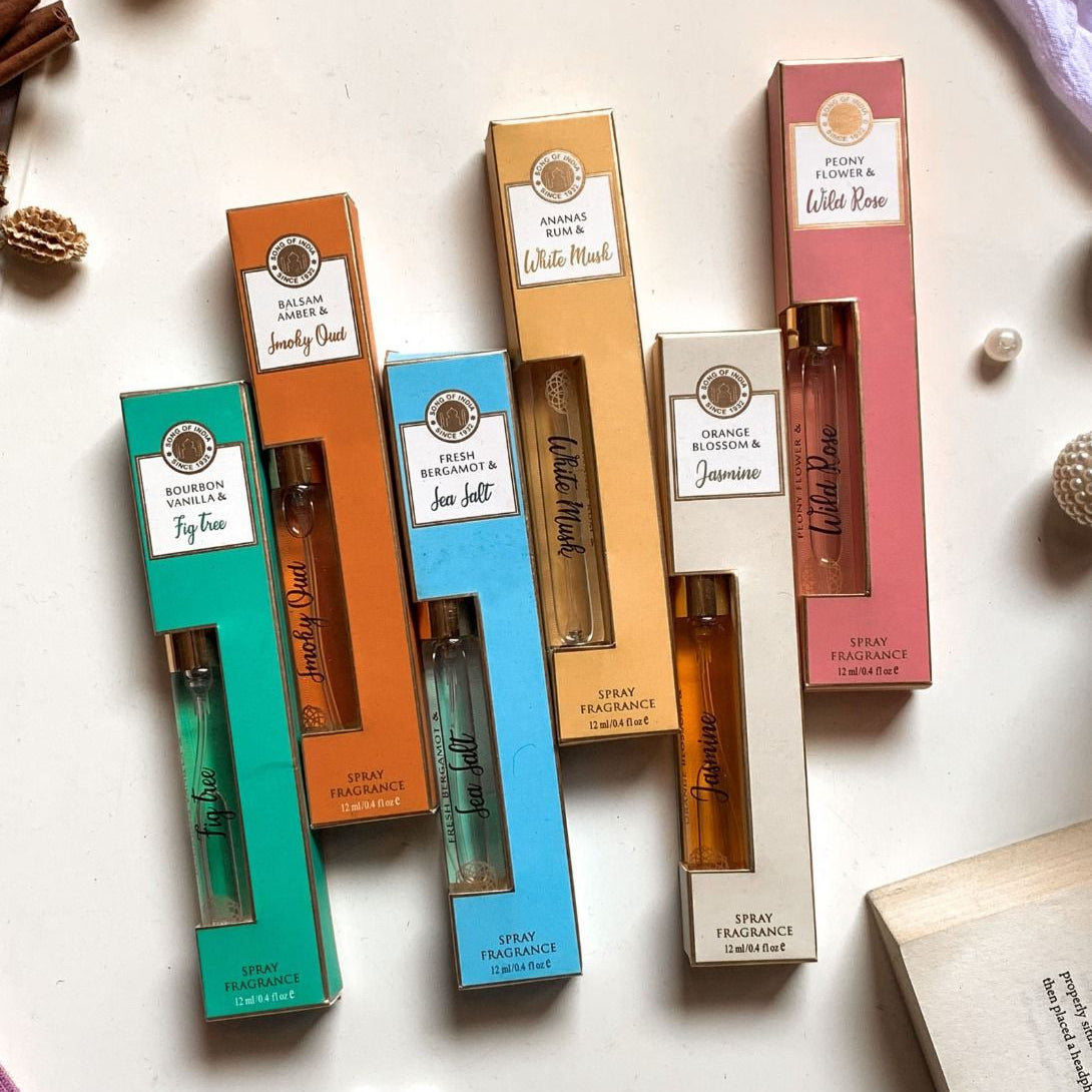 Collection of natural spray fragrances in glass bottles including Bourbon Vanilla & Fig (green), Smoky Oud (orange), Sea Salt (blue), White Musk (gold), Jasmine (white), and Wild Rose (pink).