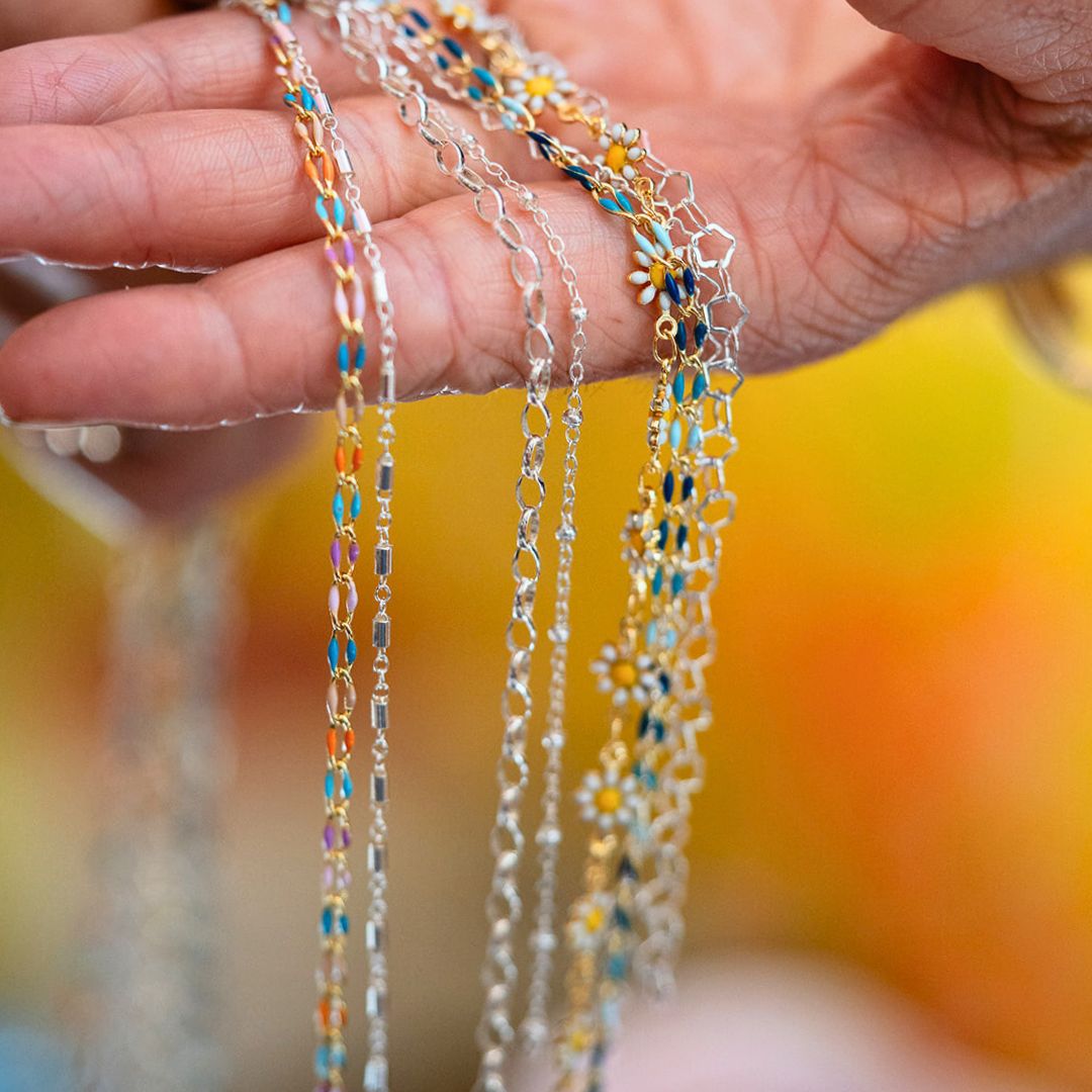 Detailed view of permanent jewelry chains and enamel work at Bella Vita - showcasing delicate sterling silver links and colorful daisy accents