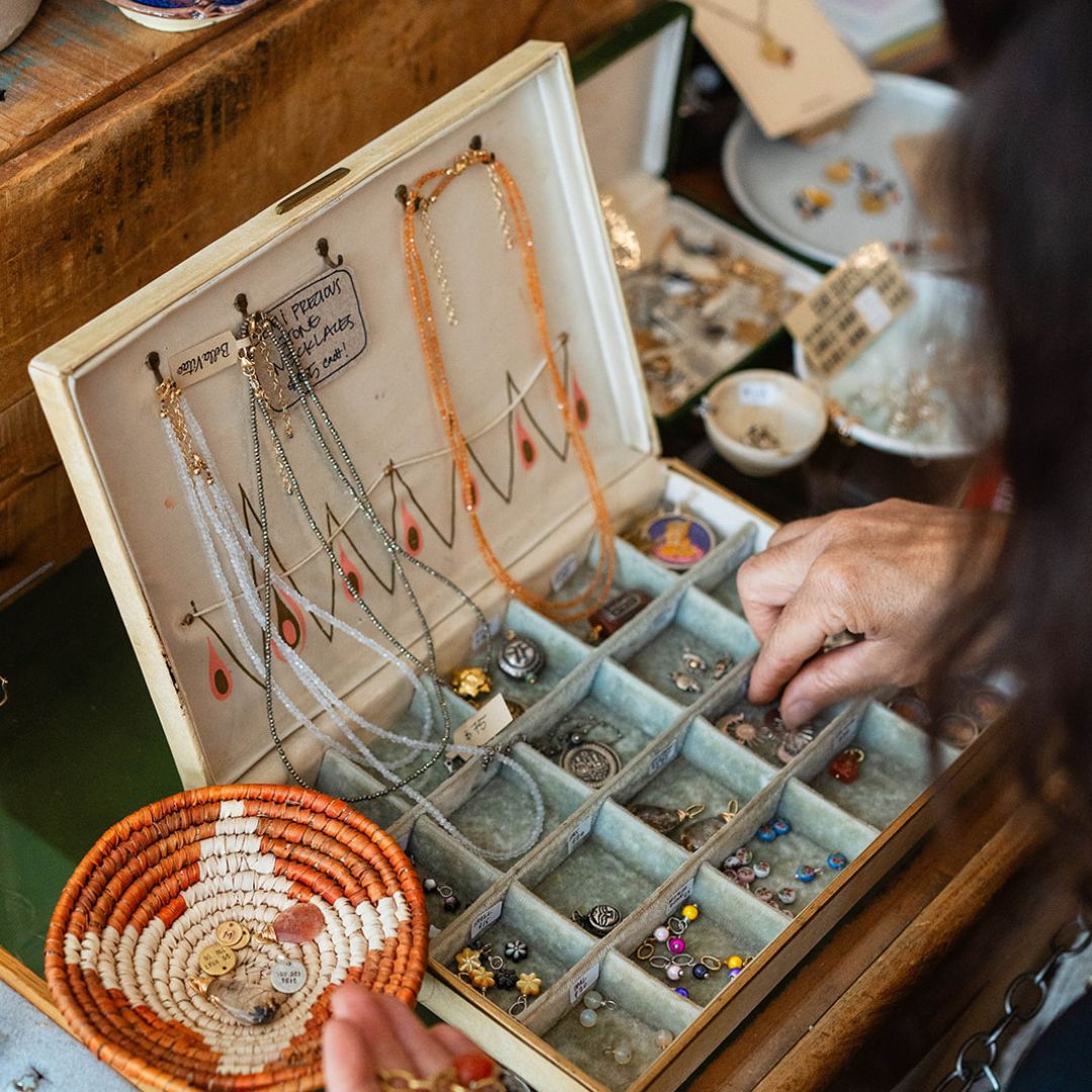 Artisan jewelry workspace showing vintage-style display box with organized charms, beads, and delicate necklaces in turquoise compartments