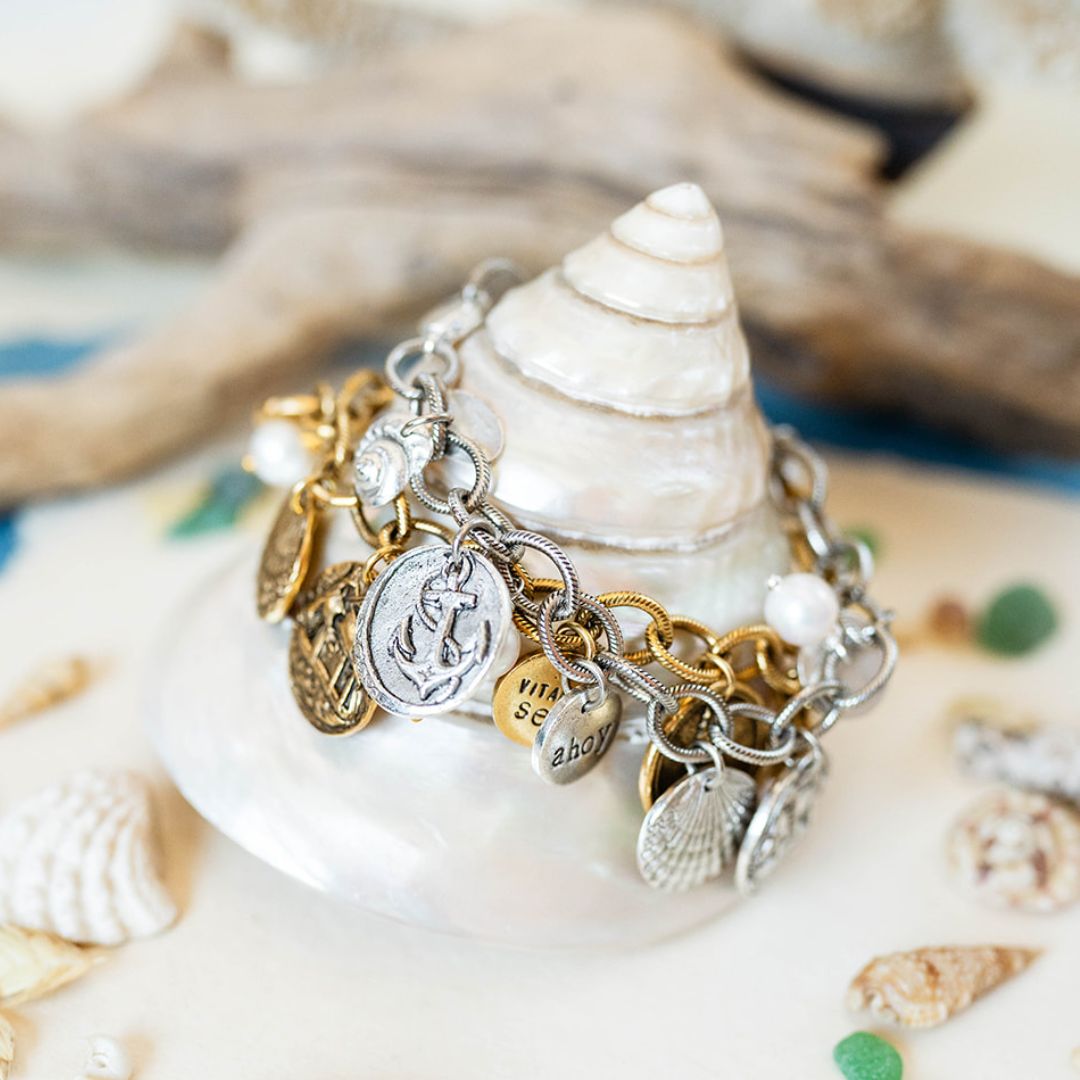 Yacht Rock charm bracelet with mixed metal nautical charms including anchor and shell motifs displayed on a conch shell