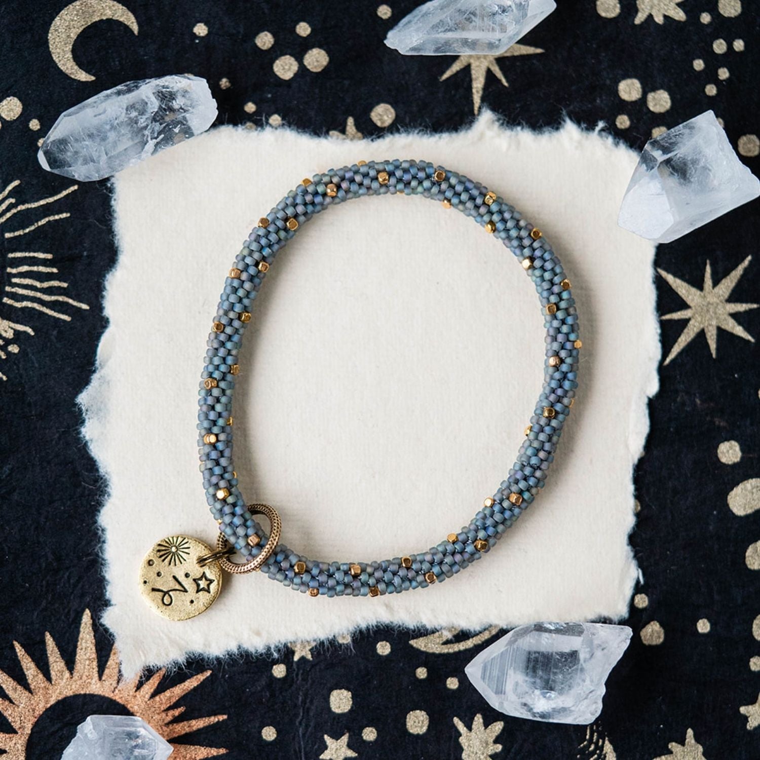 Blue-grey beaded bracelet with gold spacers and Capricorn zodiac charm on celestial background