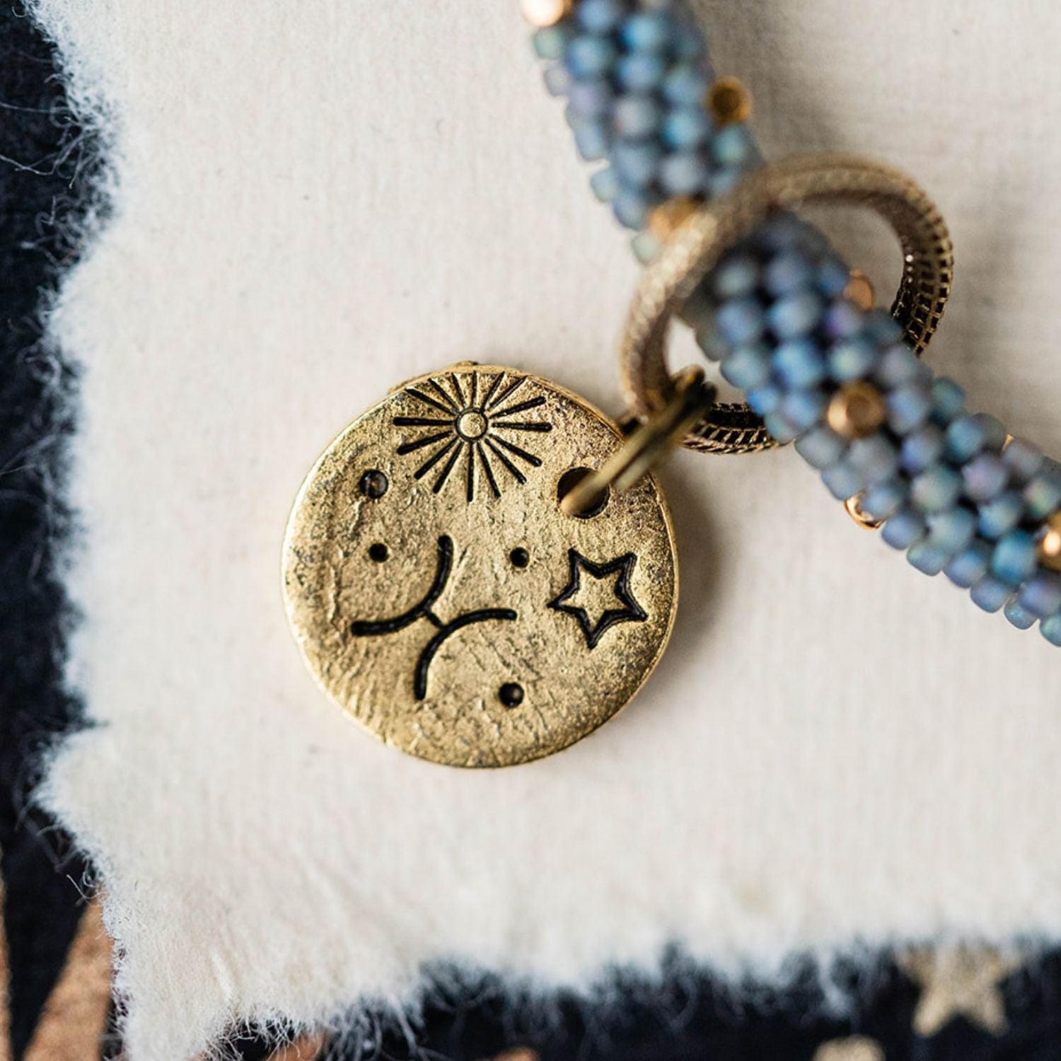 Gold Pisces charm with blue-grey beaded jewelry showing fish constellation and sun engravings
