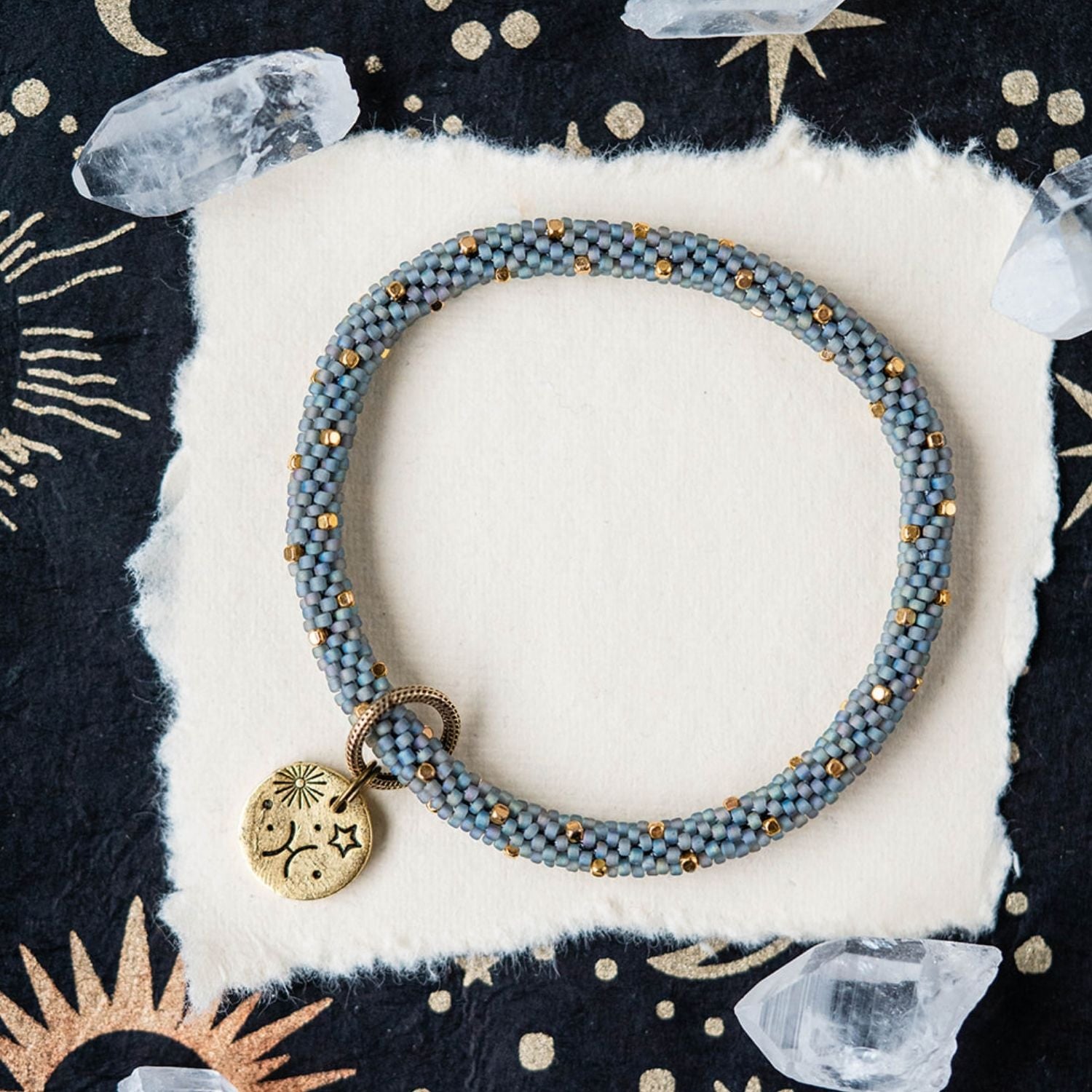 Blue-grey beaded bracelet with gold spacers and Pisces zodiac charm on starry background