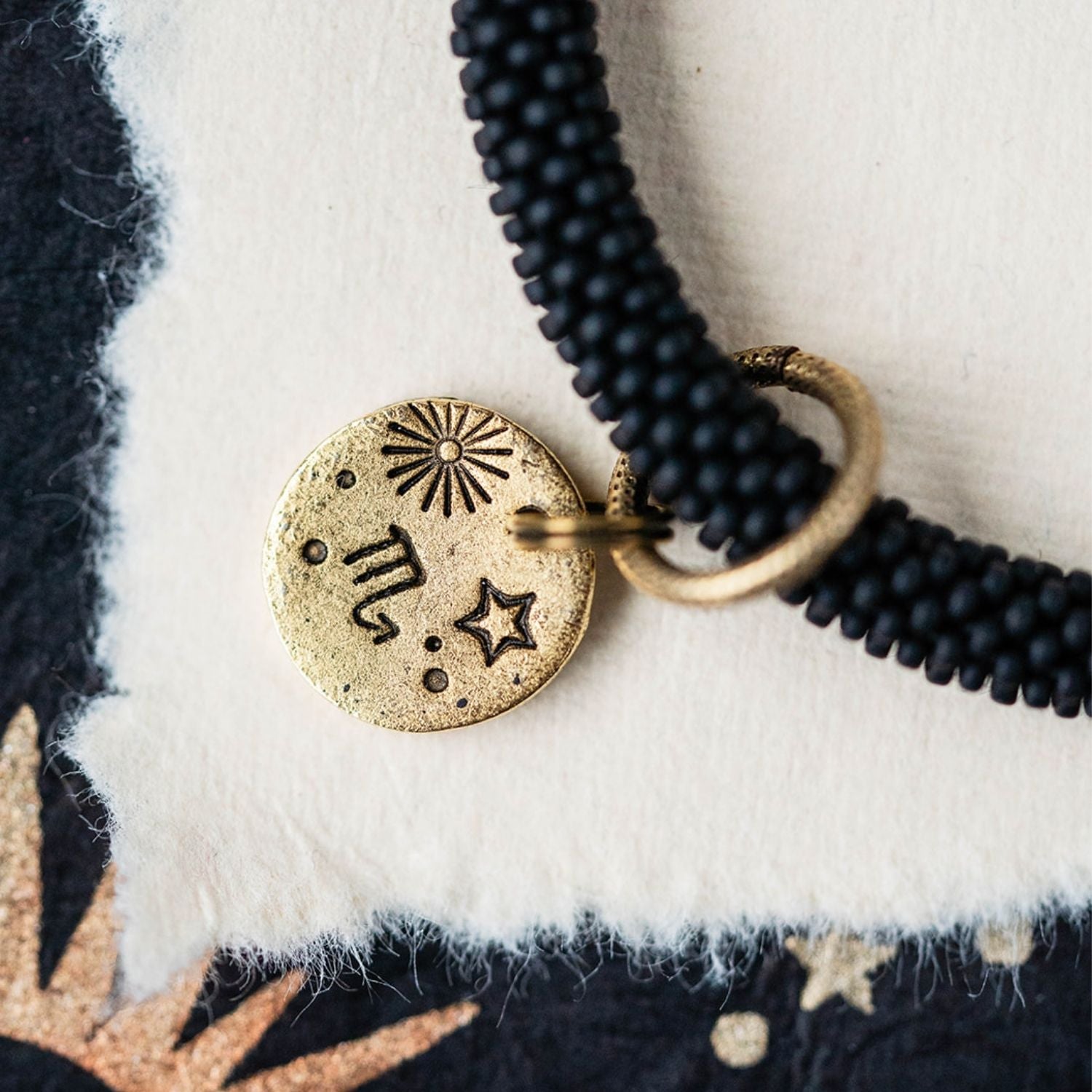 Close-up gold Scorpio zodiac charm with constellation symbols attached to black beaded bracelet