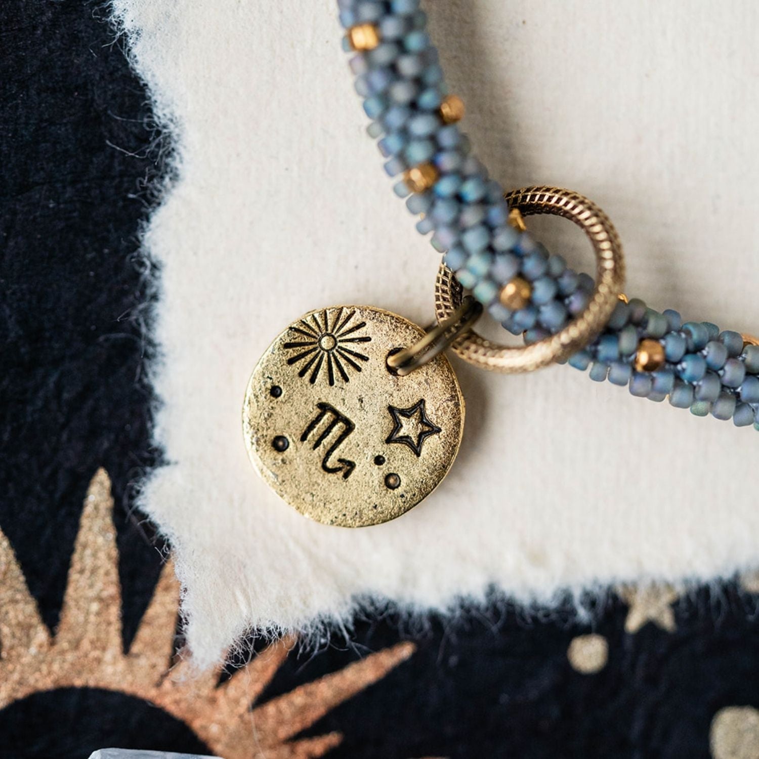 Gold Scorpio zodiac pendant with blue-grey beaded jewelry showing scorpion constellation engravings