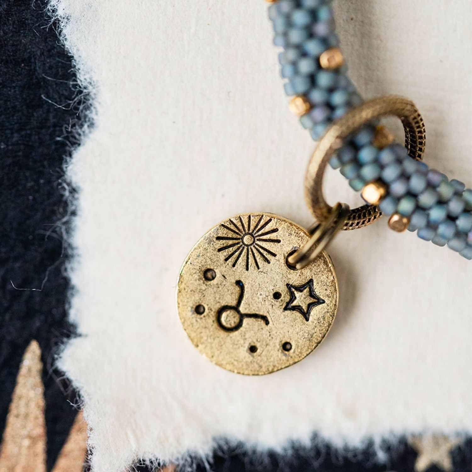 Gold Taurus charm with blue-grey beaded jewelry showing bull constellation and sun engravings