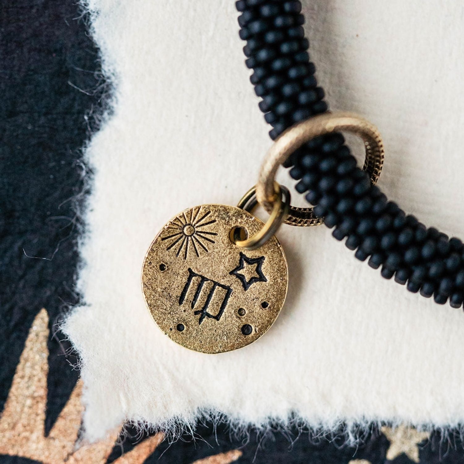 Close-up gold Virgo zodiac charm with maiden symbols attached to black beaded bracelet detail