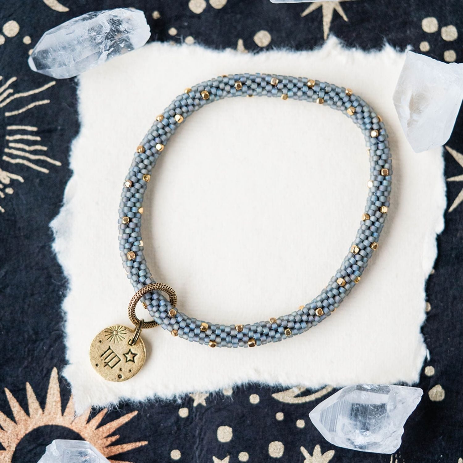 Blue-grey beaded bracelet with gold spacers and Virgo zodiac charm on starry background