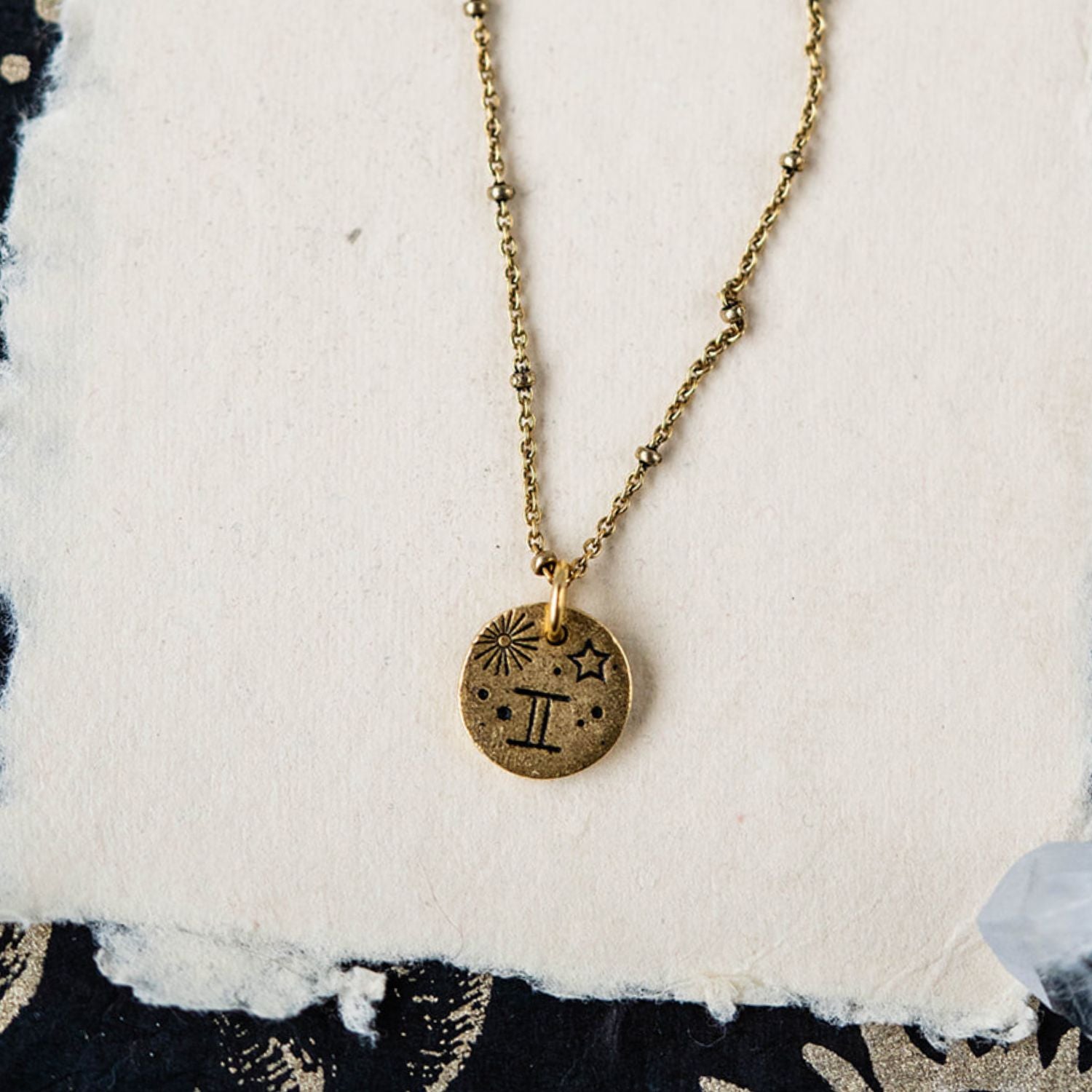 Gemini constellation charm necklace featuring gold disc with engraved twins and star motifs